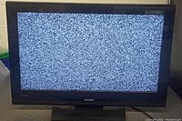 Full view of Toshiba TV front showing static noise on screen indicating power on but no signal.