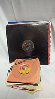 Stack of 12 inch and 45 RPM vinyl records in sleeves showing various labels and condition