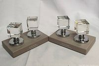 Four door knobs with clear acrylic cube handles and chrome round bases, arranged in two sets each holding two knobs, on white background.