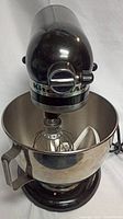 Front angle of black KitchenAid Artisan tilt-head stand mixer with stainless steel mixing bowl installed and wire whisk attached