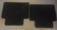 Two black fabric car mats shown on metal textured floor, one with unique shape and one rectangular.