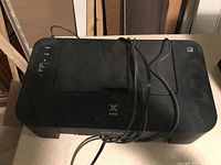 Top view of a black Canon Pixma TS202 printer/scanner with power cable on top.