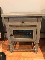 Front view of one refinished end table showing drawer and closed glass cabinet door.