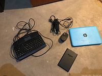 All items in the lot arranged on a beige floor showing the HP laptop, wired keyboard, wired mouse, Amazon Kindle, and power cables.