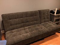 Side angle view of the grey fabric sofa bed, showing tufted backrest and seat with textured upholstery on hardwood floor.