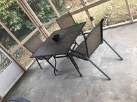 Square metal frame table with black tiled top and three matching metal mesh chairs arranged on a concrete floor in screened patio.
