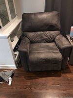 Brown fabric recliner chair positioned on hardwood floor with visible wear and pet hair.