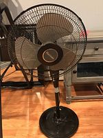 Front view of a black standing oscillating fan with beige blades on a round base, showing the Holmes brand name on the center hub.