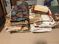 Stack of folded various patterned and colored tablecloths and placemats on a table.