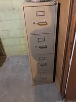 Front view of tall beige metal filing cabinet showing four drawers with handles and label holders, lock on top drawer.
