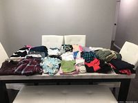 Photo showing folded assorted women's clothing in various colors and patterns on a white table with white chairs.