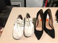 Pair of white Nike sneakers size 8 and black heels size 11 placed side by side on a beige surface.