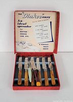 Photo showing six Dinkee table knives with brown bakelite handles and the original red box with printed interior.