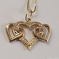 Close-up of pendant showing three interlocking heart shapes, two heart edges set with small diamonds, polished finish