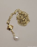 Coiled 14k gold chain with layered disc pendant and pearl drop on neutral background