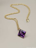 Full view of gold rope chain with purple amethyst pendant laid out flat showing clasp
