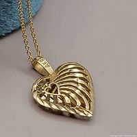 Close-up showing front side of heart pendant with intricate laser-cut design and linked chain.