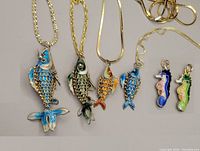 Six gold-plated sterling silver chains with cloisonné enamel sea creature pendants including fish and seahorses laid out side by side.