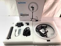 Video conferencing kit items arranged in styrofoam packaging including ring light, microphone, cables, and accessories with Safari box in background.