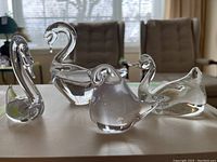 Four clear glass bird figurines arranged on a white surface showing size and shape differences.