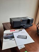 Side view of the Boston Acoustic MicroSystem radio on a wooden table with owner manual and product literature placed next to it
