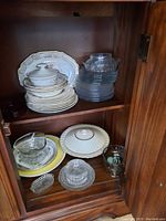 Photo of upper and lower cabinet shelves showing stacked Dominion China bowls and plates, Jlmenau clear glass plates and bowls, vintage clear glass pieces
