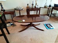 Full side view of the oval coffee table, showing the wooden top, pedestal base and legs.