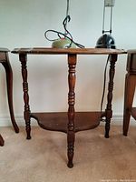 Side view of the wood demi lune side table showing turned legs and lower shelf.