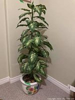 Full view of the faux leafy plant in the ceramic pot placed on carpeted floor in corner of room.