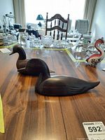 Two handcrafted dark wood duck figurines displayed on a wood table, showing side and top view with detailed carving and smooth finish.