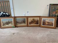 Four wood framed and matted landscape prints by Cornelius Krieghoff on the floor against a wall.