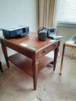 Photo of wood side table showing side angle with drawer and brass capped feet, medium brown finish.