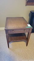 Front angled view of the vintage wood side table showing drawer and brass cap feet