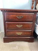 Front view of a wooden nightstand with three drawers and brass handles showing scratches on finish.