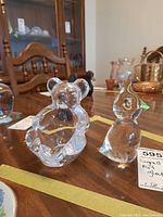Two clear art glass figurines on table, visible details of bear-shaped and bird-shaped figures.