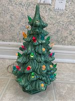 Front view of vintage green ceramic electric Christmas tree with multiple colored bulbs including red, blue, green, yellow, purple, and orange bulbs inserted in ceramic sockets. Some bulbs missing.