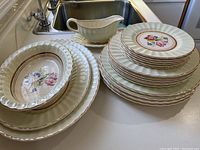 Overview of stacked plates including dinner, dessert, side plates alongside creamer and gravy boat on countertop