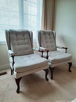 Pair of wood framed armchairs positioned near window showing front and side view, highlighting tufted upholstery and wood legs.