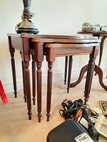 Side angle photo of the three wood nesting tables stacked within each other showing the turned legs and scalloped edges.