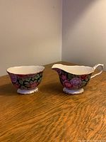 Porcelain cream pitcher and sugar bowl with floral chintz design placed on wooden surface.