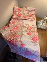 Full view of pink and green floral tablecloth laid out on table with five matching napkins folded beside it.