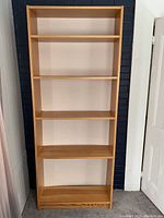 Front view of the tall wooden bookcase with five shelves, showing the natural wood finish and overall rectangular shape.