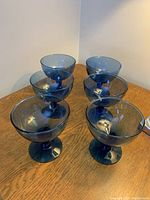 Six blue glass dessert bowls arranged on a wooden table showing their size and shape.