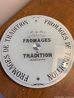 Top view of the circular glass cheese tray showing the black printed brand and decorative text.