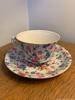 Tea cup and saucer set shown on wooden surface with floral chintz pattern and gold trim along rims.