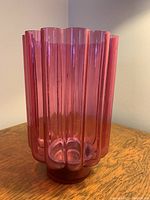 Front angled view of ribbed cranberry glass candle holder or vase showing vertical ridges and round base