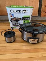 Full view of Crock-Pot Cook & Carry slow cooker next to Little Dipper food warmer and original box on wooden floor.