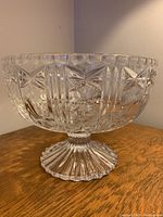 Photo showing side and partial top view of clear crystal pedestal bowl with intricate cut patterns and scalloped rim