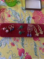 Photo of five pairs of earrings laid on a red velvet display on a colorful floral tablecloth