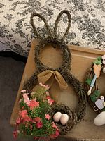 Rabbit-shaped wreath with bunny ears, pink flowers, and two small speckled eggs in nest area